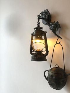 an old fashioned teapot hanging on the wall next to a light fixture with a candle in it