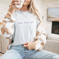 a woman sitting on a couch holding a doughnut in her hand and wearing a sweater that says code your asf