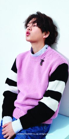 a young man sitting on top of a white bench wearing a pink and black sweater