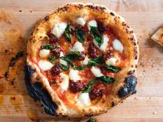 a pizza sitting on top of a wooden table covered in cheese and spinach leaves