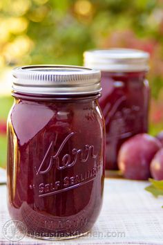 two jars filled with red liquid sitting on top of a table next to apples and grapes