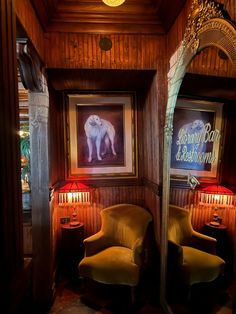 two yellow chairs sitting in front of a painting on the wall next to a lamp