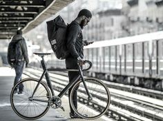 a man standing next to a train station with his bike and looking at his cell phone