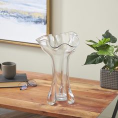 a clear glass vase sitting on top of a wooden table next to a potted plant