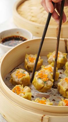 a person holding chopsticks over dumplings in a wooden container with other food items