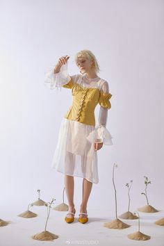 a woman in a yellow top and white skirt standing next to some small flower stems