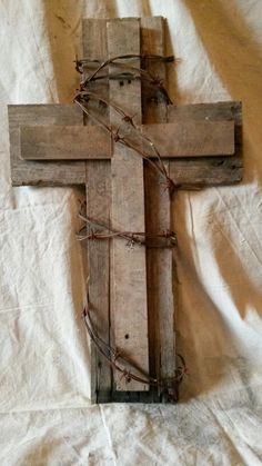 a wooden cross with barbed wire around it on a white sheeted surface in front of a wall