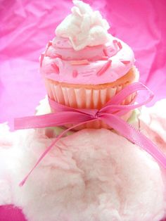 a pink cupcake sitting on top of a pile of white fluffy balls and ribbons