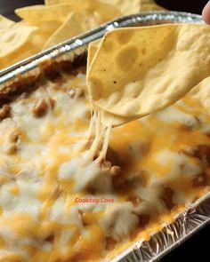 a hand holding a tortilla chip and dipping it into a casserole