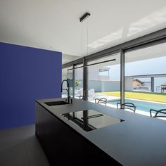 an empty kitchen with blue walls and black counter tops next to a swimming pool in the background