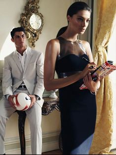 a man and woman standing next to each other in front of a window with a clock on the wall