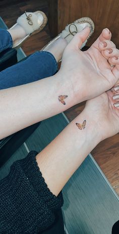 two women holding hands with butterfly tattoos on them