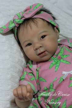 a baby doll that is laying down on a white blanket wearing a pink and green outfit