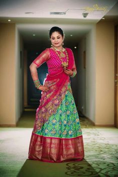 a woman in a green and pink lehenga standing on a carpeted hallway