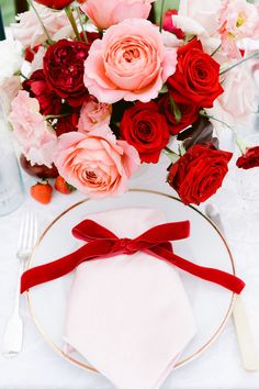 a white plate topped with a red bow next to a vase filled with pink and red flowers