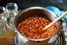 a pot filled with chili and corn on top of a wooden table next to glasses