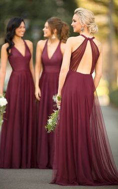 three bridesmaids in maroon dresses are standing on the street and looking at each other