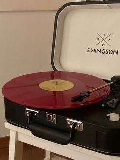 a red and black record player sitting on top of a white table next to a suitcase