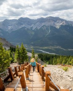 a woman walking across a wooden bridge on top of a mountain