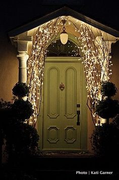 a green door is lit up with christmas lights in front of it and an arch over the doorway