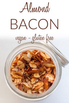 a glass jar filled with bacon on top of a white table next to a spoon