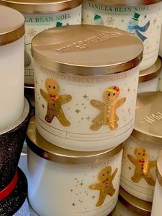 several candles are stacked on top of each other in gold and white tins with gingerbread characters