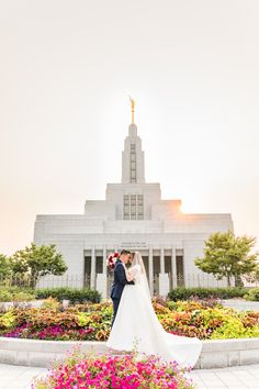 a bride and groom standing in front of the mormon temple at sunset with flowers all around them