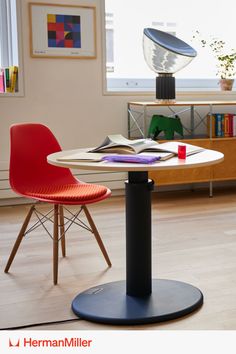 An OE1 Sit-to-Stand Table with a book on it, next to a red chair. Industrial Facility, Polished Aesthetic