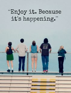 four people standing on a fence with the words enjoy it because it's happening