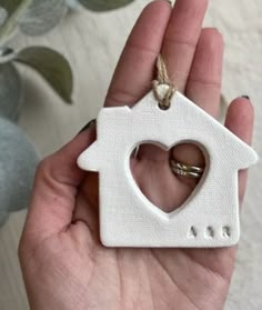 a hand holding a white ceramic house ornament with a heart in the shape of a house