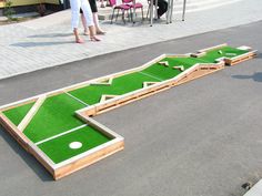 a miniature golf course on the street with people walking around and one person standing next to it