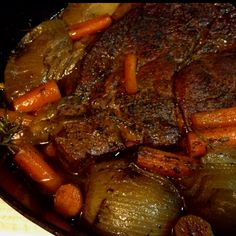 some meat and carrots are cooking in a skillet on the stove with broth