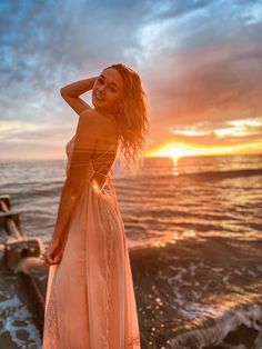 a woman standing on top of a beach next to the ocean with her hands behind her head