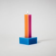 a single lit candle sitting on top of a blue block in front of a white background