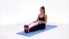 a woman sitting on a yoga mat holding a pink and black exercise tube in her right hand