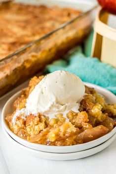 a white bowl filled with apple cobbler next to a pan of baked bread and ice cream