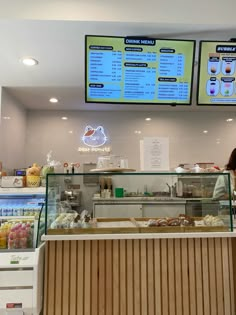 a woman standing in front of a counter at a bakery with menus on the wall