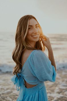 a woman standing on top of a beach next to the ocean wearing a blue dress