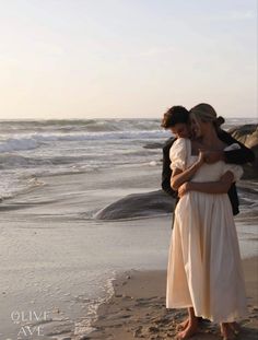 two people standing on the beach hugging each other