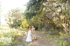 a bride and groom walking through the woods