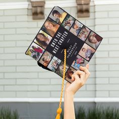 a person holding up a book with pictures on it in front of a white brick building