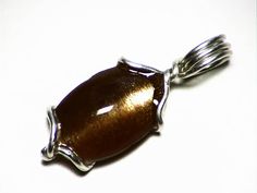 This pendant features a cabochon of Tanzanian golden star sunstone. The stone measures 0.59 x 0.36 inches (15.1 x 9.3 mm) and weighs in at 5.3 carats. Sunstone is a variety of gem feldspar, the family that also includes moonstone--it is defined by having reflective inclusions that give it both sheen and color. There are several varieties, but Tanzania produces a particularly fine variety sometimes called confetti or illusion sunstone. This variety actually has a moonstone base with a silvery adu Spiritual Brown Cabochon Jewelry, Brown Cabochon Pendant Jewelry, Silver Cat Eye Jewelry Gift, Silver Cat Eye Jewelry For Gift, Sunstone Jewelry, Fossil Teeth, Peridot Crystal, Fossil Jewelry, Peridot Jewelry