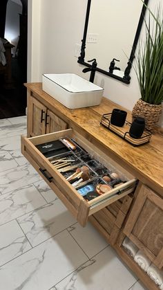 an open drawer in the middle of a wooden cabinet next to a sink and mirror