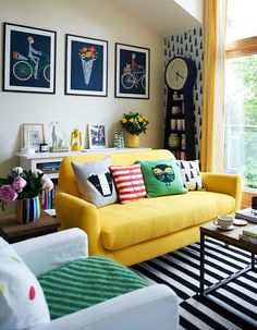 a living room with yellow couches and pictures on the wall above them, along with other furniture