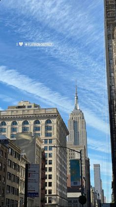 a city street filled with lots of tall buildings under a blue sky covered in wispy clouds