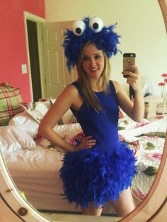 a woman taking a selfie in front of a mirror wearing a blue feathered dress