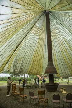 people are standing under an umbrella with chairs around it