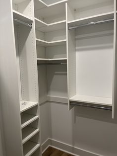 an empty walk in closet with white shelving and wood flooring on the side