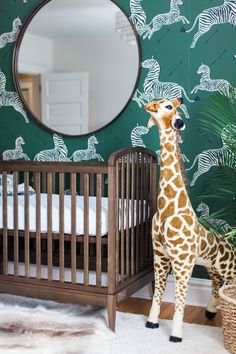 a giraffe standing next to a baby crib in front of a mirror