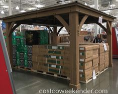 a large wooden gazebo in a warehouse with boxes on the floor and people walking around